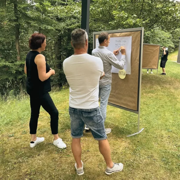 Drei Personen stehen in der Natur vor einer Tafel und machen darauf Notizen.